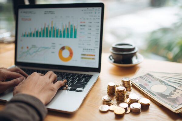 Modern çalışma alanında finansal gösterge ekranı, kahve ve Japon yenleriyle uluslararası para transferi ve tasarruf konseptli ofis ortamı.